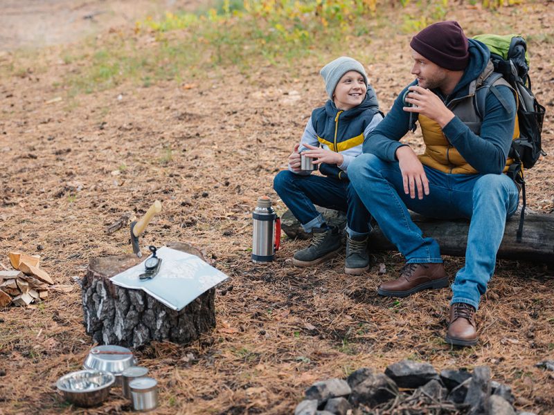 high angle view of happy father and son drinking tea from thermos in forest